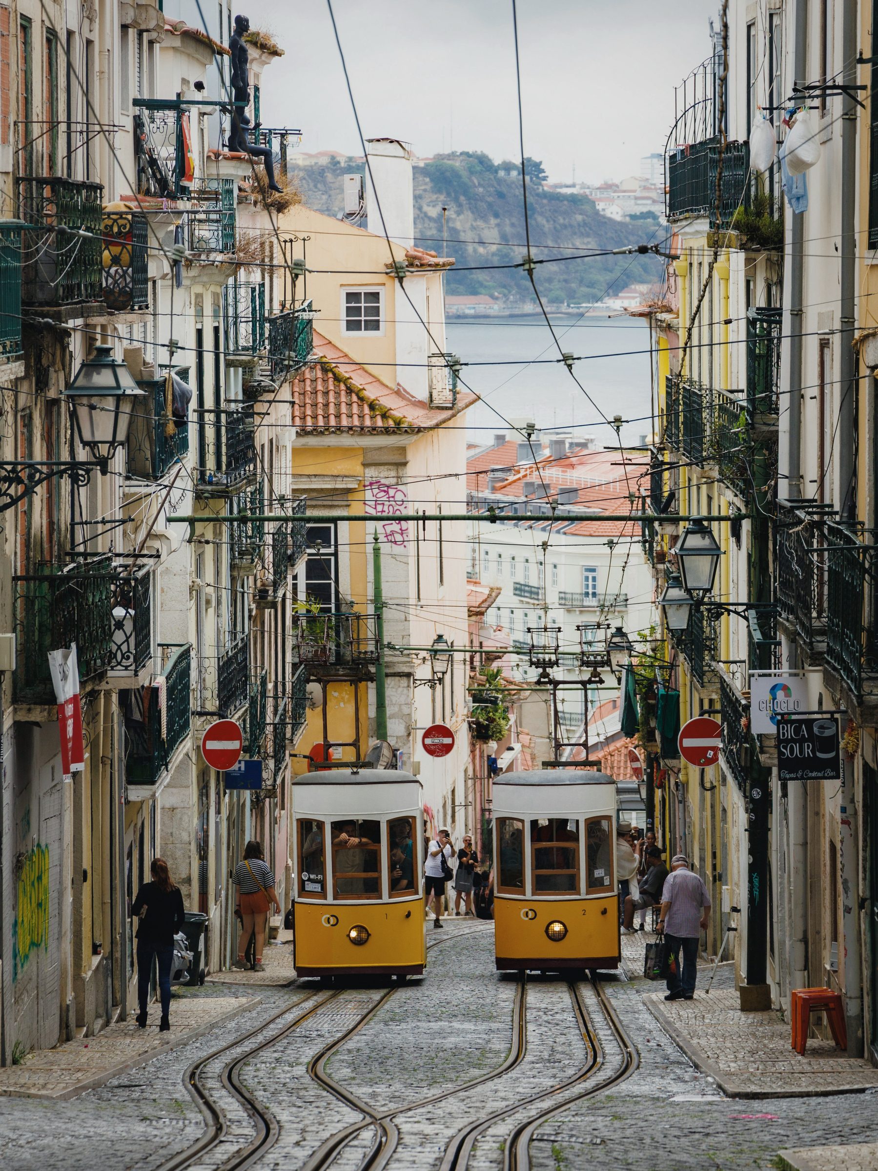 Two yellow trams passing on a steep Lisbon street above the Tagus.